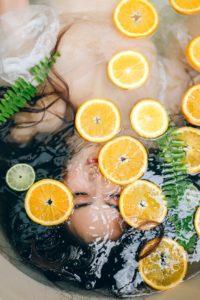 A woman relaxing in a bathtub filled with water and sliced lemons, enjoying a refreshing soak as part of her body skin care routine for dry skin