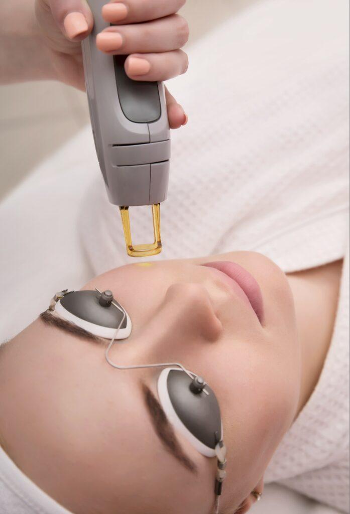 Therapist beautician makes a laser treatment to young womans face at beauty SPA clinic › Hellenic Laser Spa Woman undergoing laser treatment as part of non-surgical facial rejuvenation to smooth wrinkles and improve skin texture.