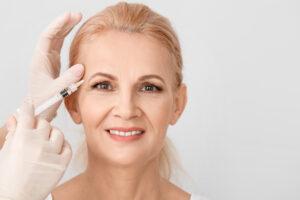 Mature woman receiving anti-aging injection in her face against light background › Hellenic Laser Spa