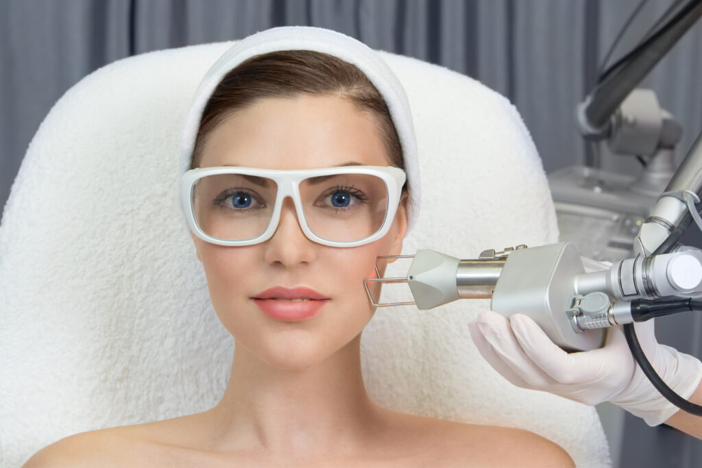 Therapist beautician makes a laser rejuvenation for the model by apparatus in a beauty salon › Hellenic Laser Spa A licensed aesthetic therapist performing a CO2 fractional laser rejuvenation procedure on a client in a professional beauty clinic treatment room.