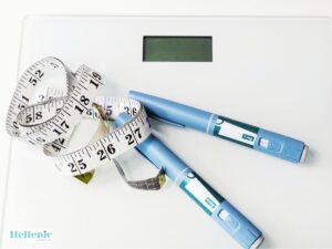 Weight Loss Injection 1 › Hellenic Laser Spa › Hellenic Laser Spa Weight loss or diabetes theme: blue insulin pens with a measuring tape on a white scale surface, suggesting medical management.